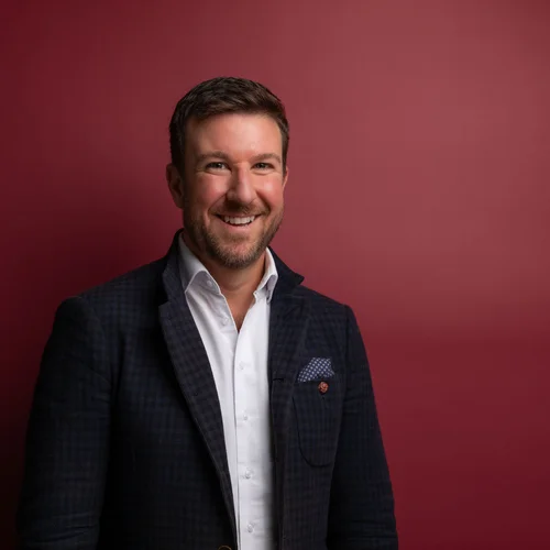 Schlosshotel Day Spa Lächelnder Mann in weißem Hemd und dunklem Sakko vor rotem Hintergrund