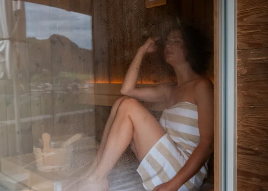In Kitzbühel ein Hotel mit Pool, bitte. Frau entspannt in der Sauna auf einem Handtuch umgeben von Holz
