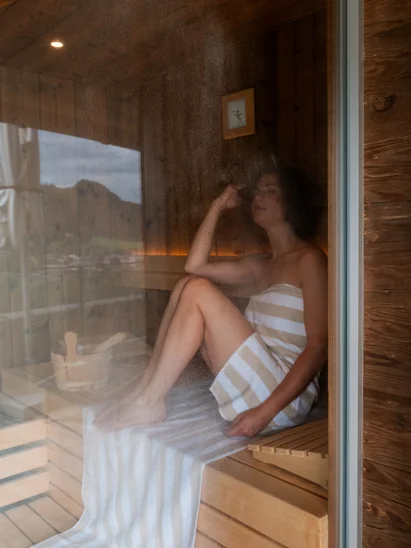 Premium-Spa im Wellnesshotel in Kitzbühel Frau entspannt in der Sauna auf einem Handtuch umgeben von Holz