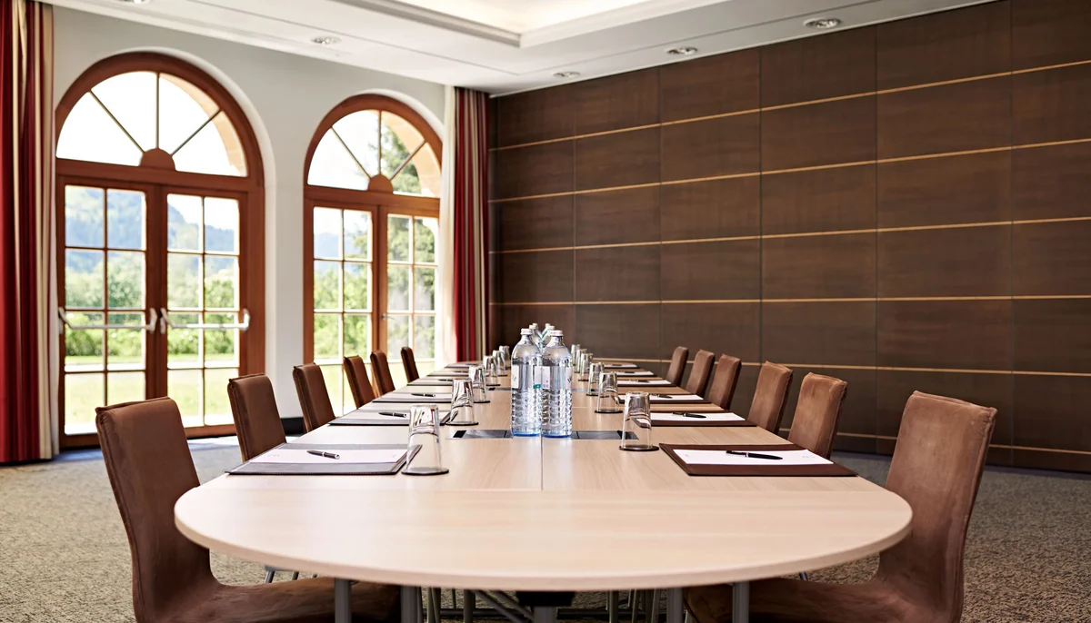 Ihr Firmenevent oder Meeting im Schlosshotel Kitzbühel Konferenzraum mit langem Tisch, Stühlen, Wasserflaschen und großen Fensterbögen