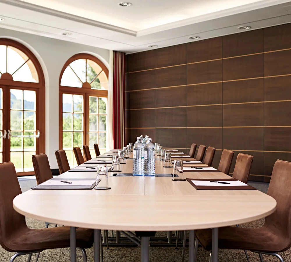 Ihr Firmenevent oder Meeting im Schlosshotel Kitzbühel Konferenzraum mit langem Tisch, Stühlen, Wasserflaschen und großen Fensterbögen
