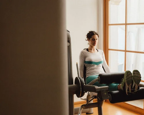 Schlosshotel Kitzbühel – un’esperienza deluxe Donna si allena con macchina per gambe, uomo la assiste come allenatore