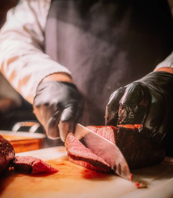 Restaurant Kitzbühel | Genuss im Schlosshotel Person schneidet gekochtes Fleisch mit Messer auf Holzbrett