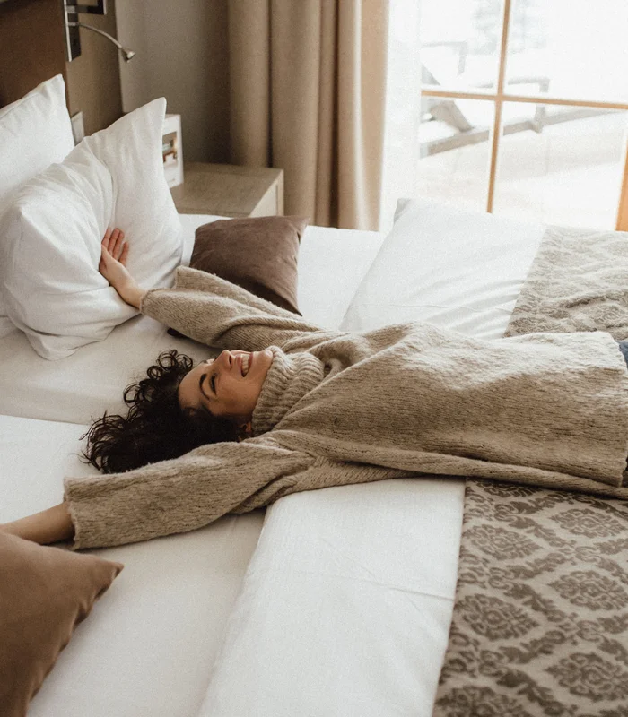 Da ist mehr drin. Frau liegt entspannt auf einem gemütlichen Bett mit hellen Kissen
