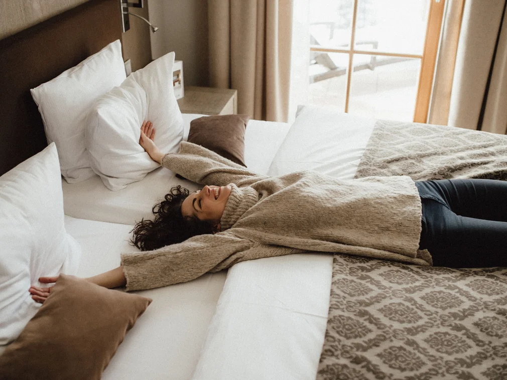 Bilder, die Sie sehen müssen. Frau liegt entspannt auf einem gemütlichen Bett mit hellen Kissen