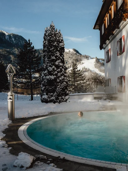 In Kitzbühel ein Hotel mit Pool, bitte. Außenpool mit dampfendem Wasser in verschneiter Winterlandschaft vor Bergkulisse