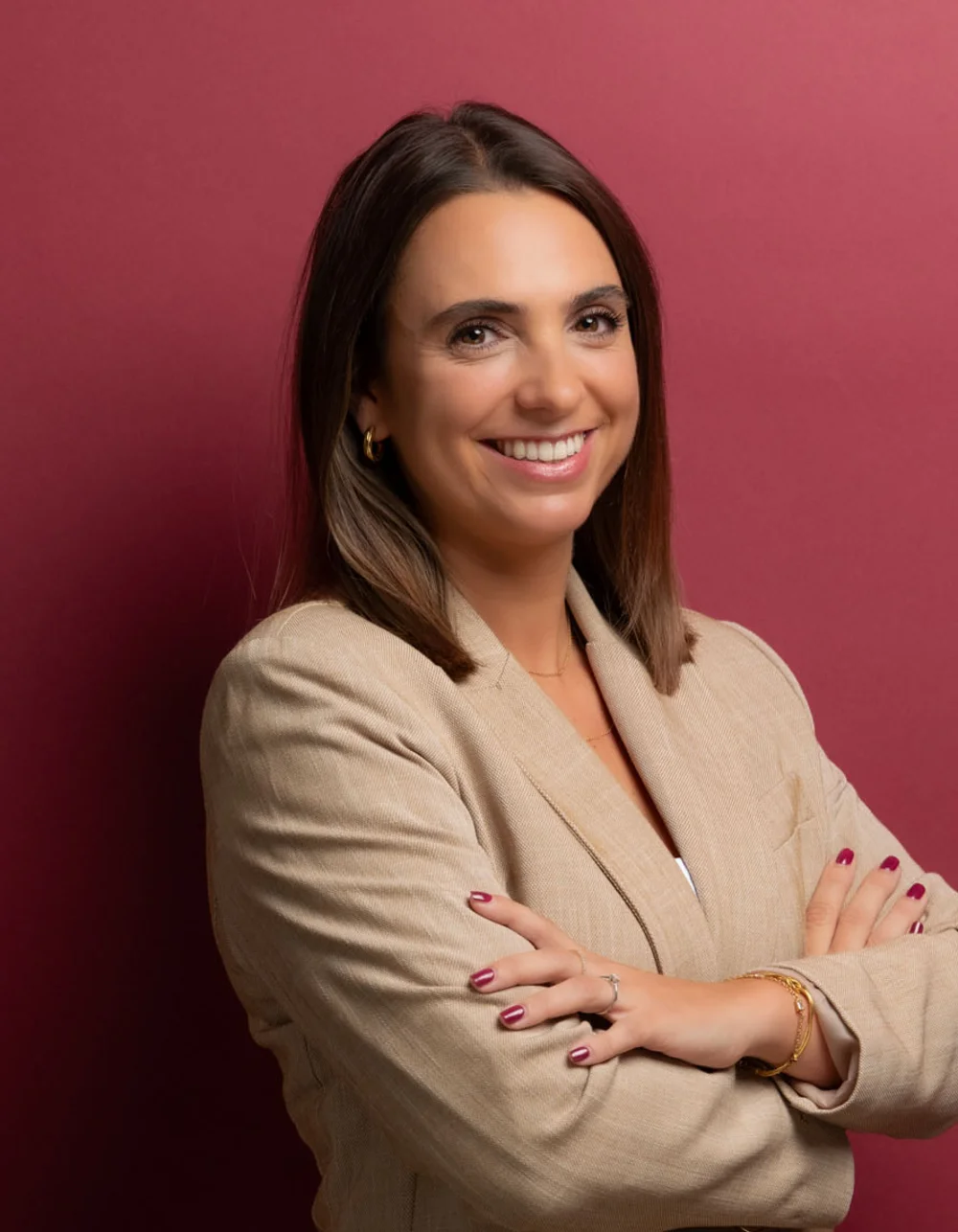 Was zählt, sind die Menschen. Frau im beigen Blazer mit verschränkten Armen vor roter Wand