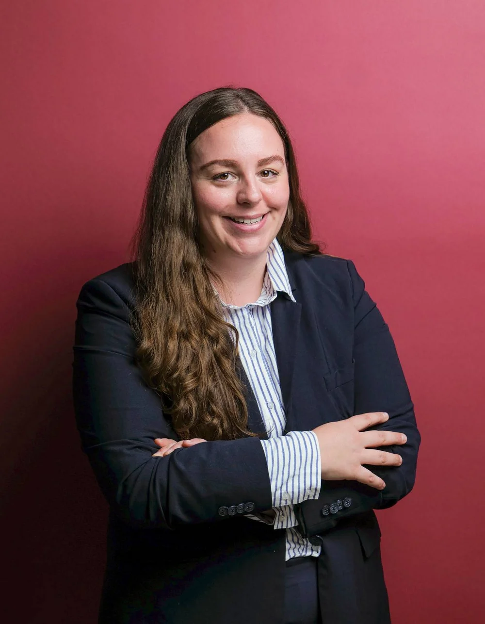 Was zählt, sind die Menschen. Frau in dunklem Anzug vor rotem Hintergrund mit verschränkten Armen