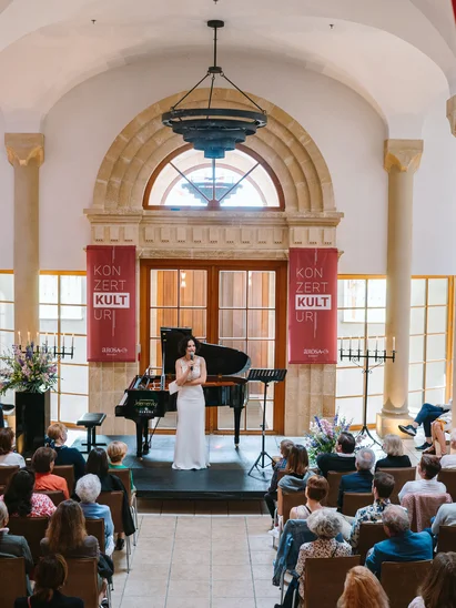 Kulturhotel. Schlosshotel. Kitzbühel. Konzertsaal mit Sängerin vor Klavier und Publikum hinter roten Vorhängen