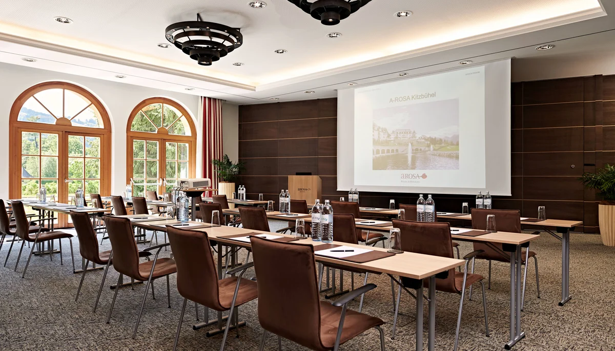 Ihr Firmenevent oder Meeting im Schlosshotel Kitzbühel Konferenzraum mit Stühlen, Tischen, Projektor und großem Bildschirm