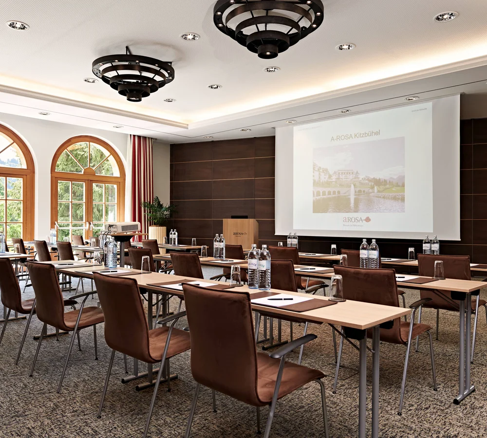 Ihr Firmenevent oder Meeting im Schlosshotel Kitzbühel Konferenzraum mit Stühlen, Tischen, Projektor und großem Bildschirm