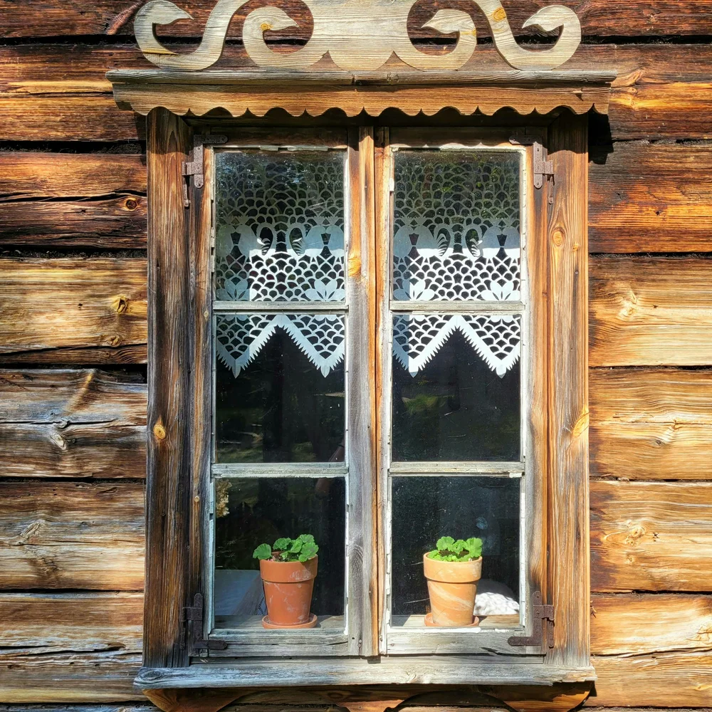 Kulturhotel. Schlosshotel. Kitzbühel. Holzfenster mit Spitze und zwei Blumentöpfen vor Holzwand