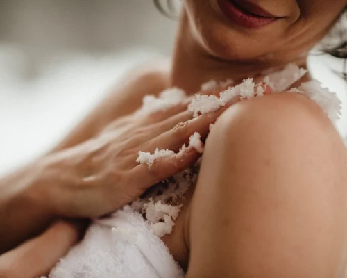 Übernachten in Kitzbühel – Zimmer und Suiten im Schlosshotel Frau cremt ihre Schulter mit Körperpeeling im Badezimmer ein