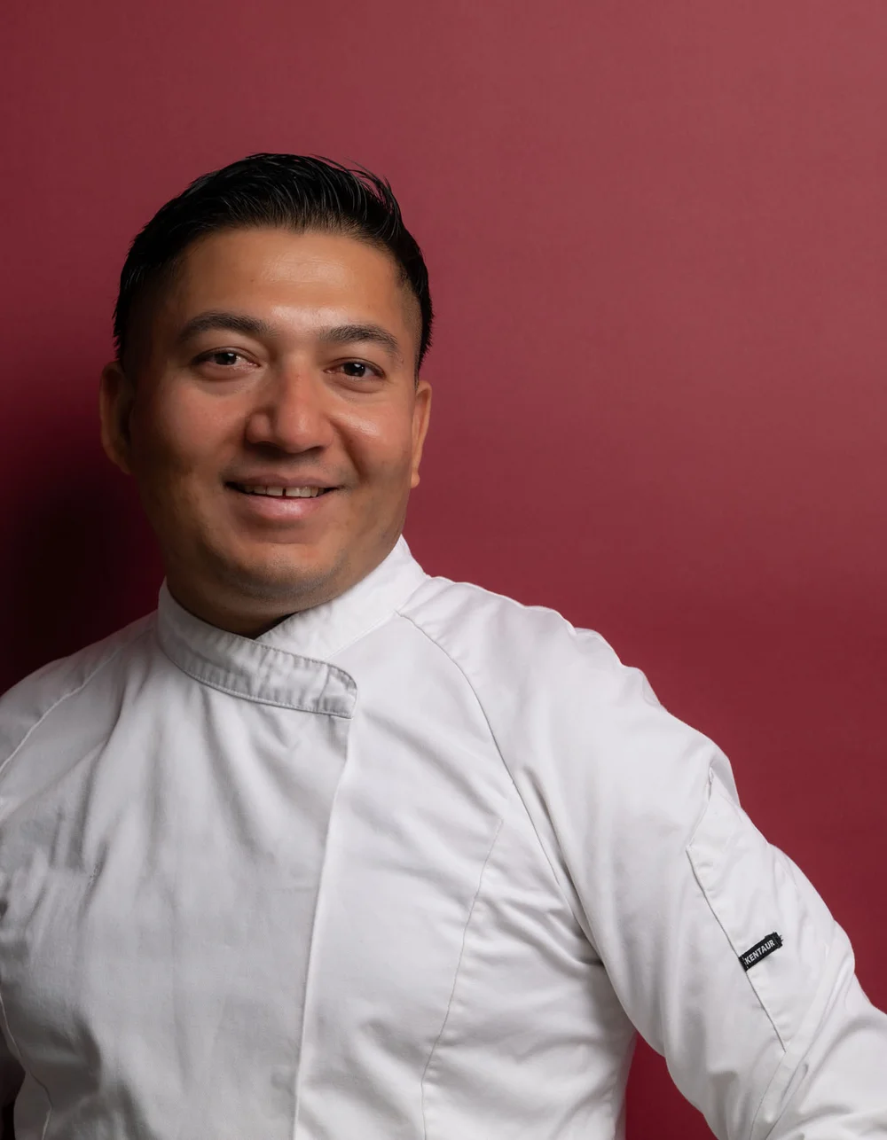 Was zählt, sind die Menschen. Porträt eines lächelnden Kochs in weißer Uniform vor rotem Hintergrund