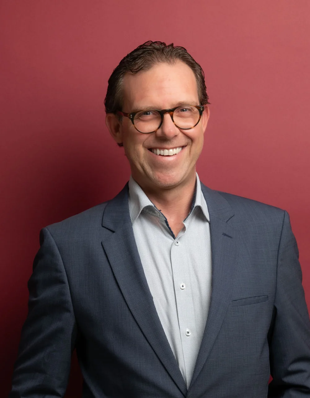 Was zählt, sind die Menschen. Lächelnder Mann in Brille und Anzug vor rotem Hintergrund