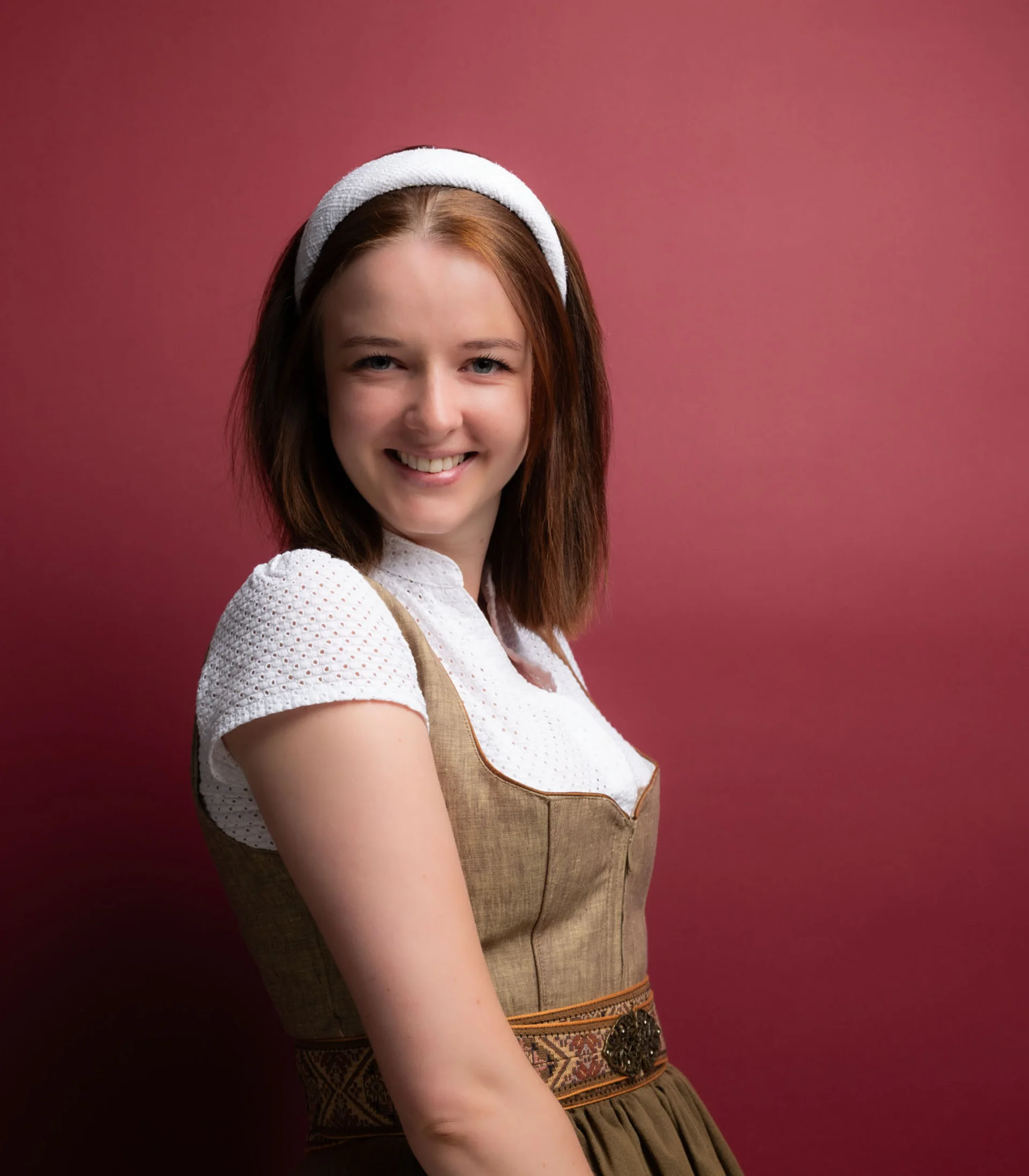 Mit besten Empfehlungen aus dem Schlosshotel Junge Frau in traditionellem Dirndl vor rotem Hintergrund