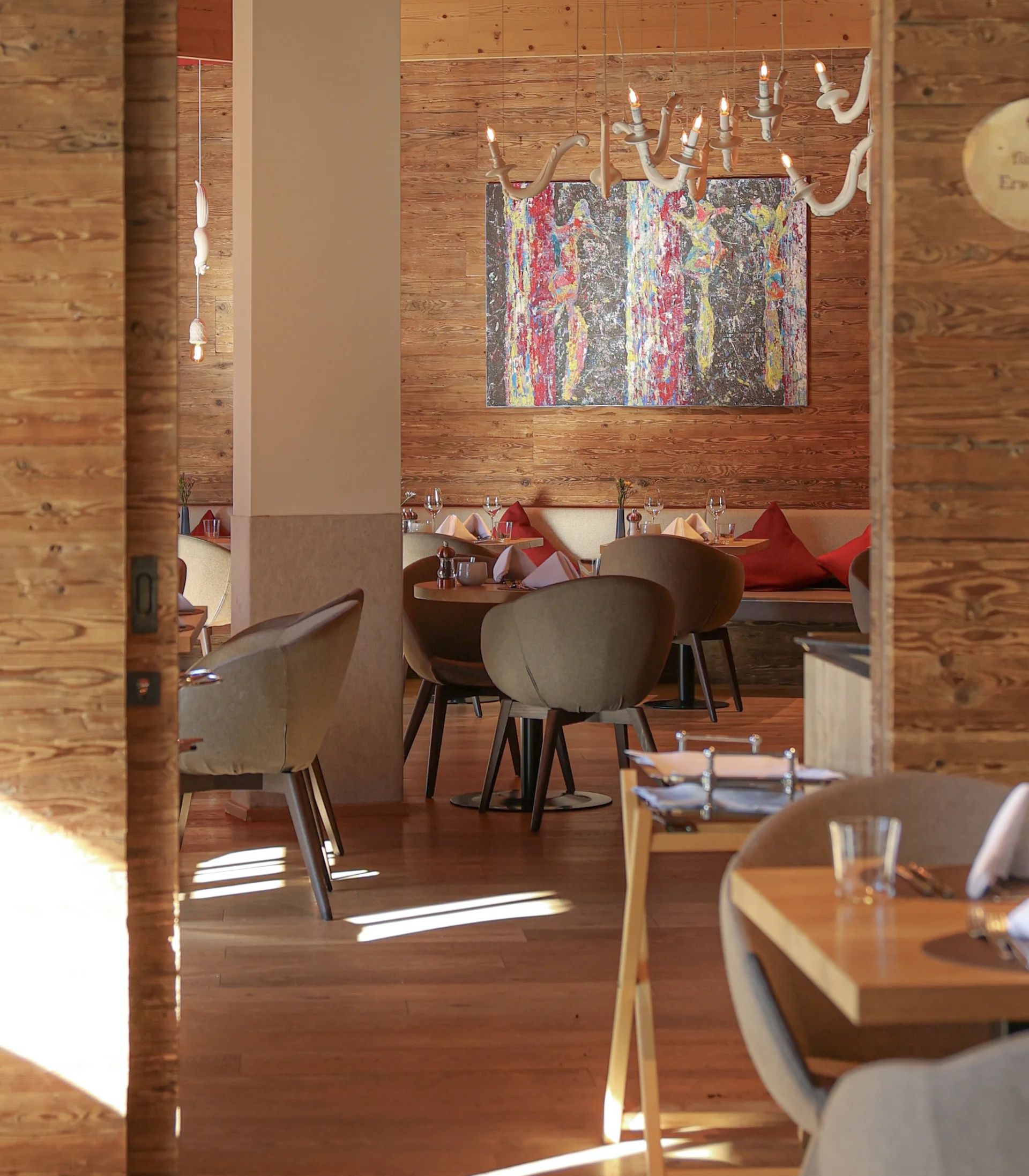 Restaurant Kitzbühel | Genuss im Schlosshotel Moderner Gastraum mit Holzwänden, dekorativen Leuchten und buntem Wandbild
