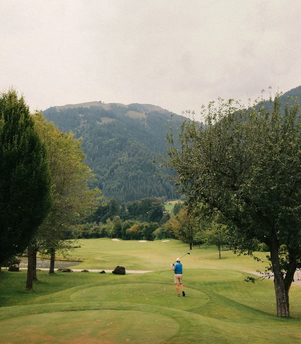 Das Golfhotel in Kitzbühel Golfer spielt auf grünem Golfplatz mit Bergen im Hintergrund
