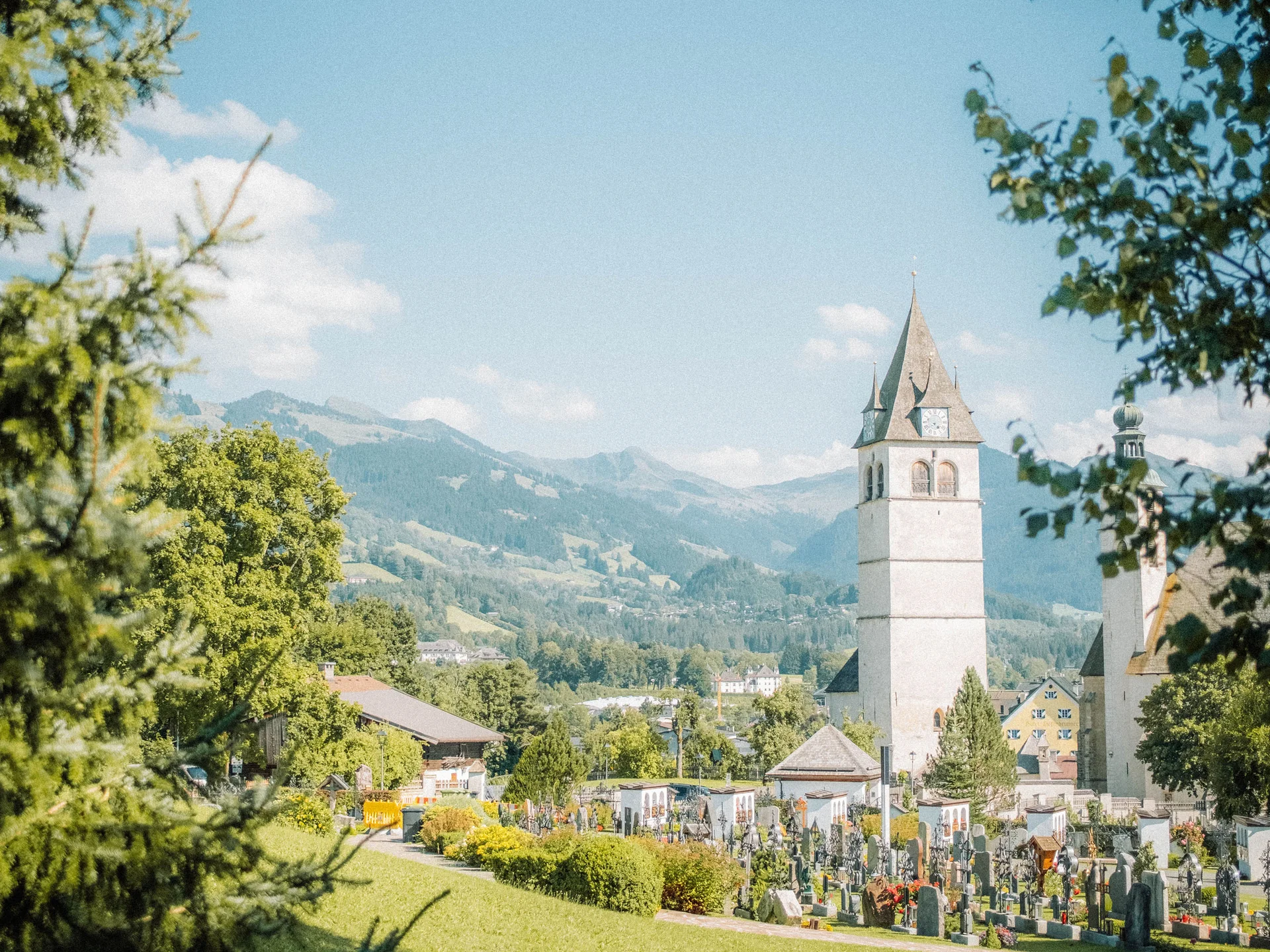 Bilder, die Sie sehen müssen. Kirchturm und Friedhof in grüner Landschaft mit Bergen im Hintergrund