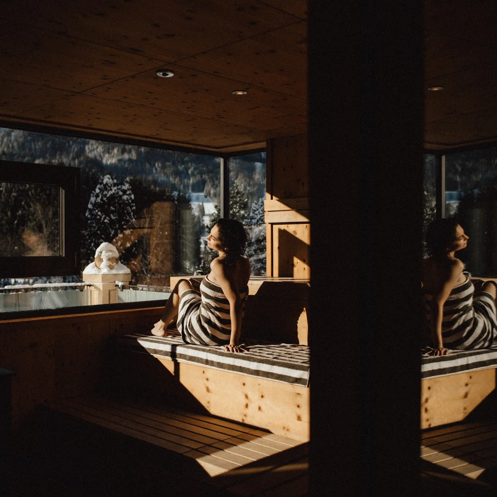 Premium-Spa im Wellnesshotel in Kitzbühel Frau sitzt in Sauna mit Handtuch und blickt auf winterliche Landschaft