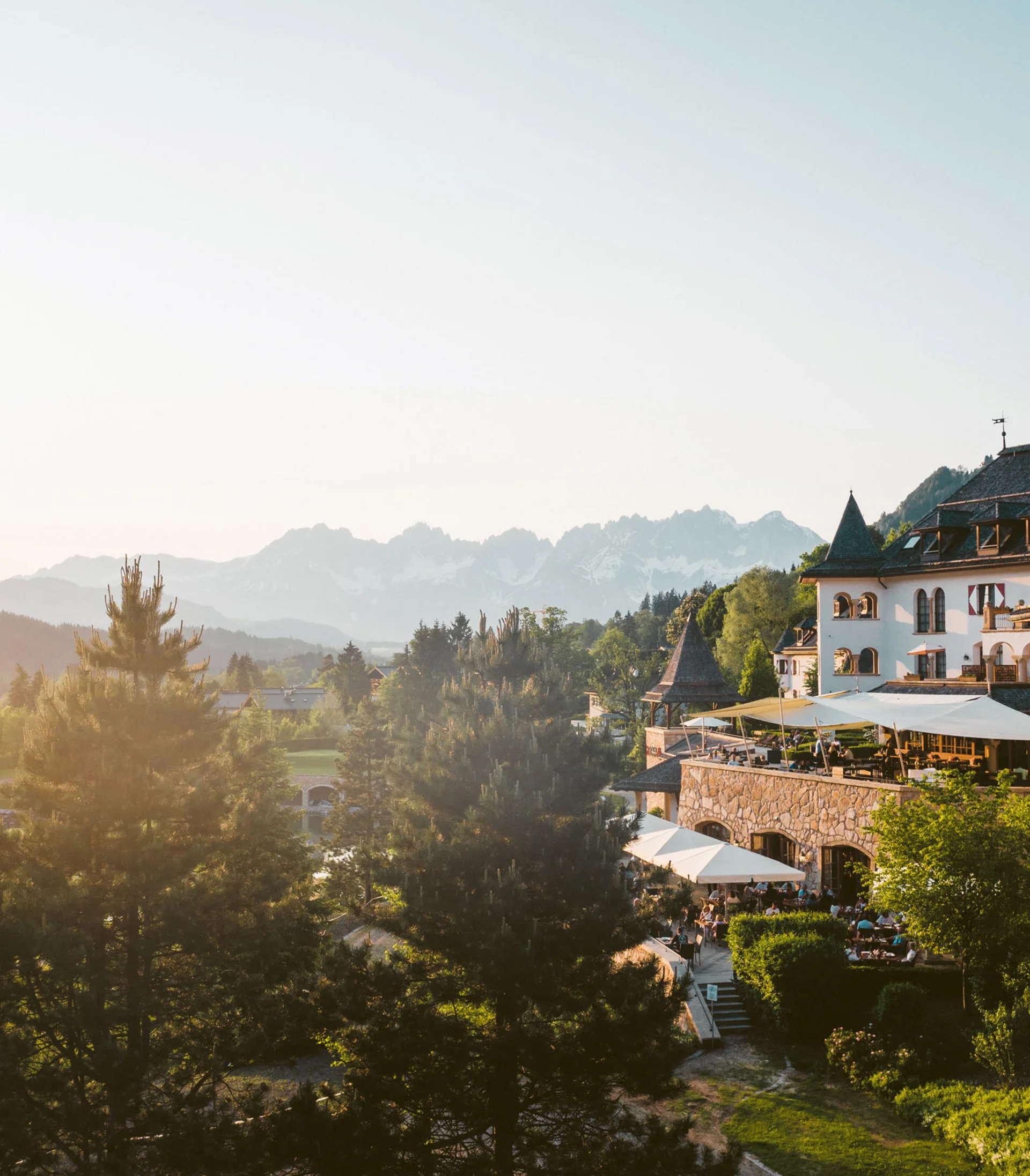 Eine der schönsten Hochzeitslocations in Tirol Blick auf ein altes Hotel mit Terrasse und Berglandschaft im Sonnenuntergang