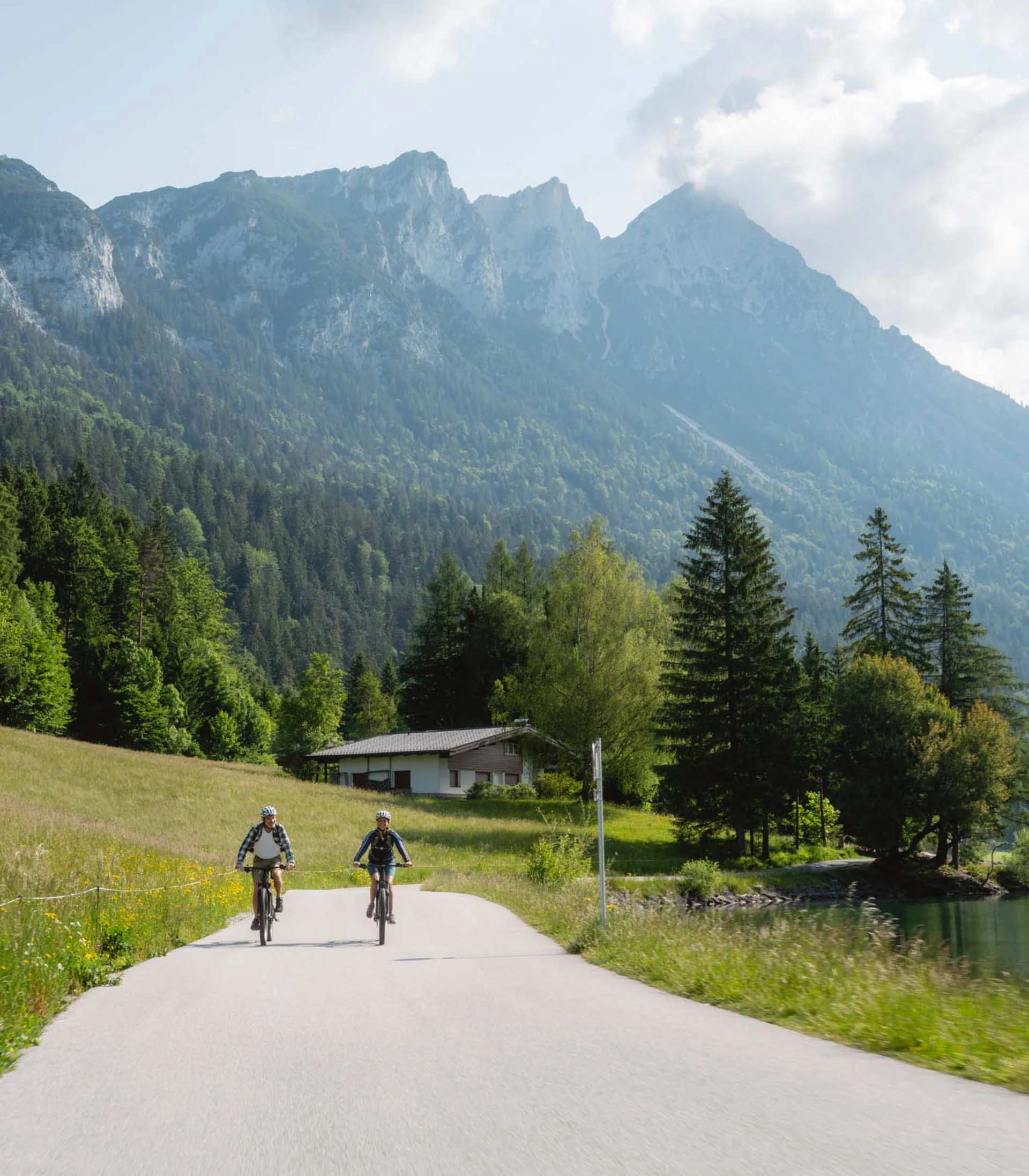 Rund ums Bikehotel in Kitzbühel wandern Zwei Radfahrer fahren auf Straße neben See mit Bergen im Hintergrund