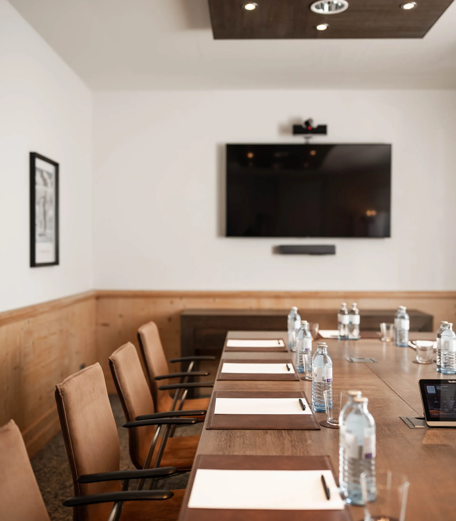 Exklusiv tagen im Seminarhotel in Tirol Konferenzraum mit vorbereitetem Tisch, Stühlen, Wasserflaschen und großem Bildschirm