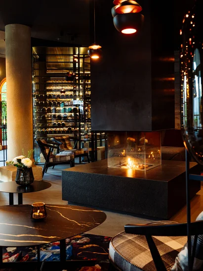 Hotel mit Klavier und Livemusik | Die Bar im Schlosshotel Kitzbühel Gemütliche Lounge mit Kamin, modernen Tischen und Stühlen im Abendlicht