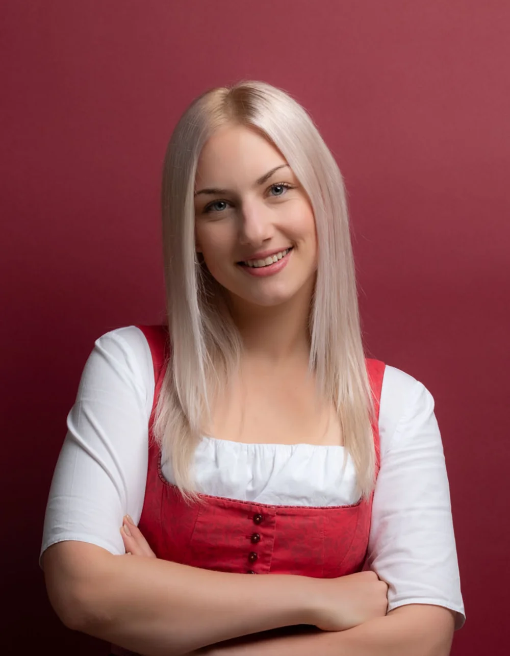 Was zählt, sind die Menschen. Junge Frau im Trachtenkleid vor rotem Hintergrund lächelnd mit verschränkten Armen