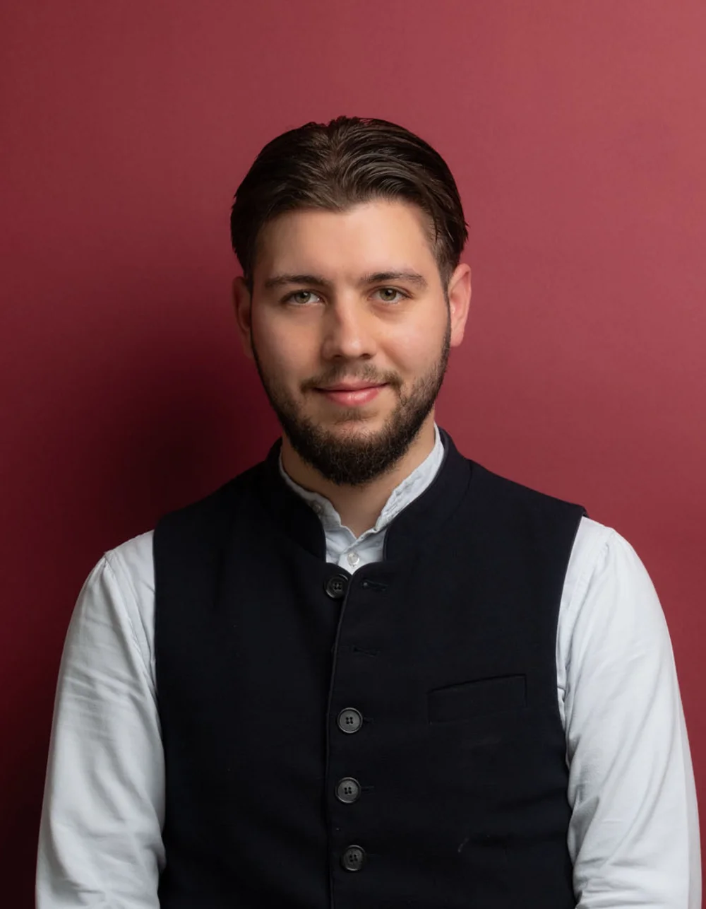 Was zählt, sind die Menschen. Junger Mann mit Hemd und schwarzer Weste vor rotem Hintergrund