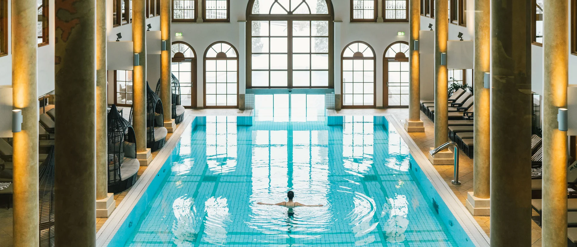 In Kitzbühel ein Hotel mit Pool, bitte. Innenaufnahme eines Schwimmbads mit Säulen und einer Person im Wasser
