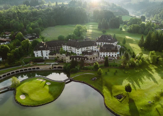 Ihre Karriere im Schlosshotel Kitzbühel Luftaufnahme eines Hotels neben einem See und Golfplatz in einer grünen Landschaft