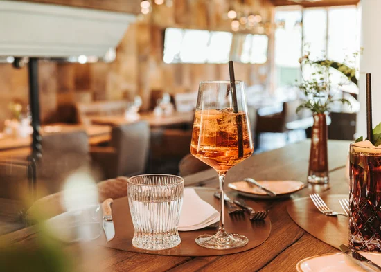 Restaurant Kitzbühel | Genuss im Schlosshotel Getränke mit Strohhalm auf einem Restauranttisch mit Besteck und Serviette