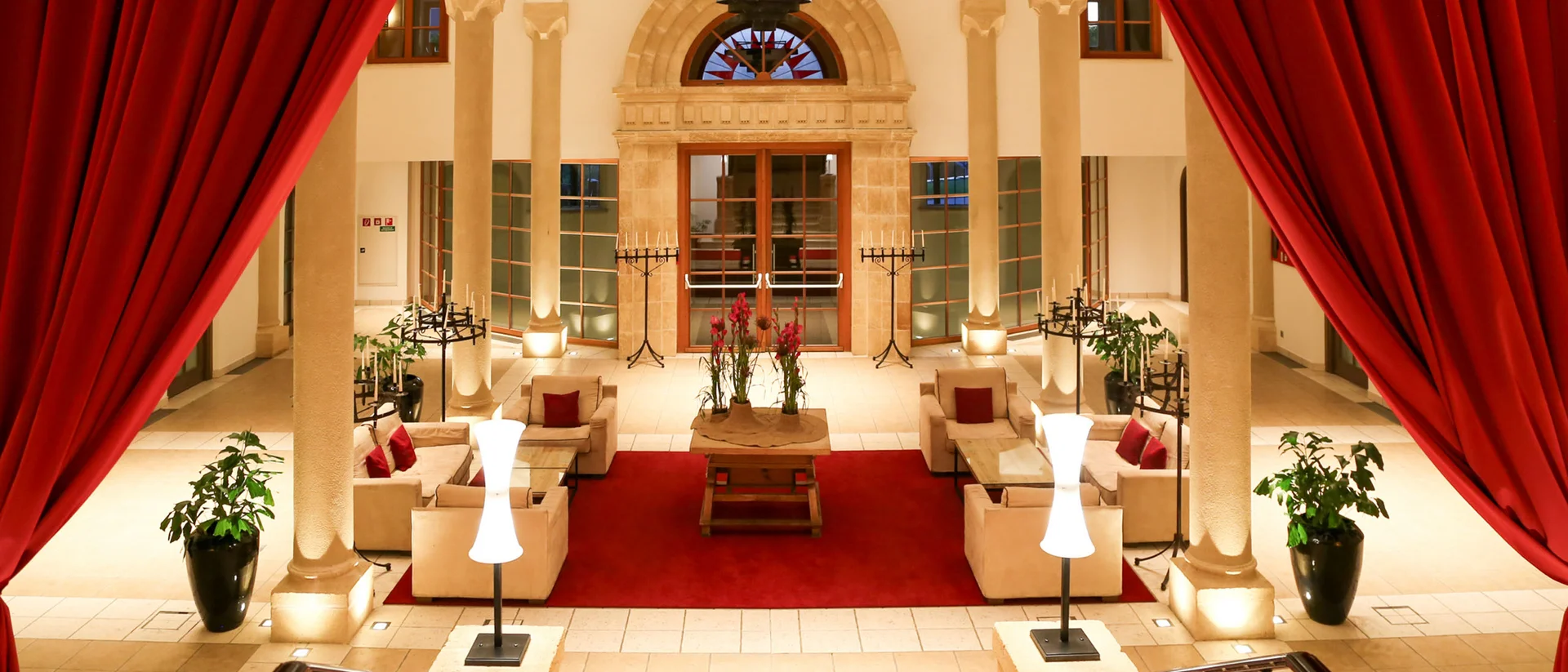 Mit besten Empfehlungen aus dem Schlosshotel Elegante Hotellobby mit roten Vorhängen und beiger Polstermöbel