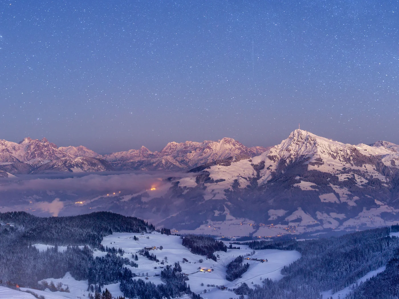 Berge in der Dämmerung Schneebedeckte Berge mit Sternenhimmel und Lichtern im Tal