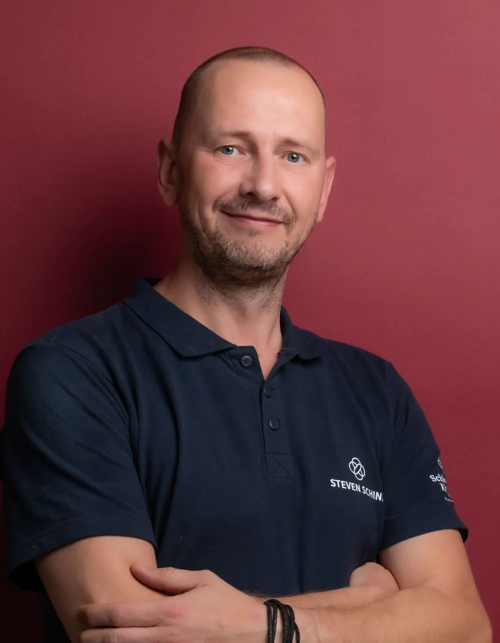 Was zählt, sind die Menschen. Mann steht vor rotem Hintergrund mit verschränkten Armen