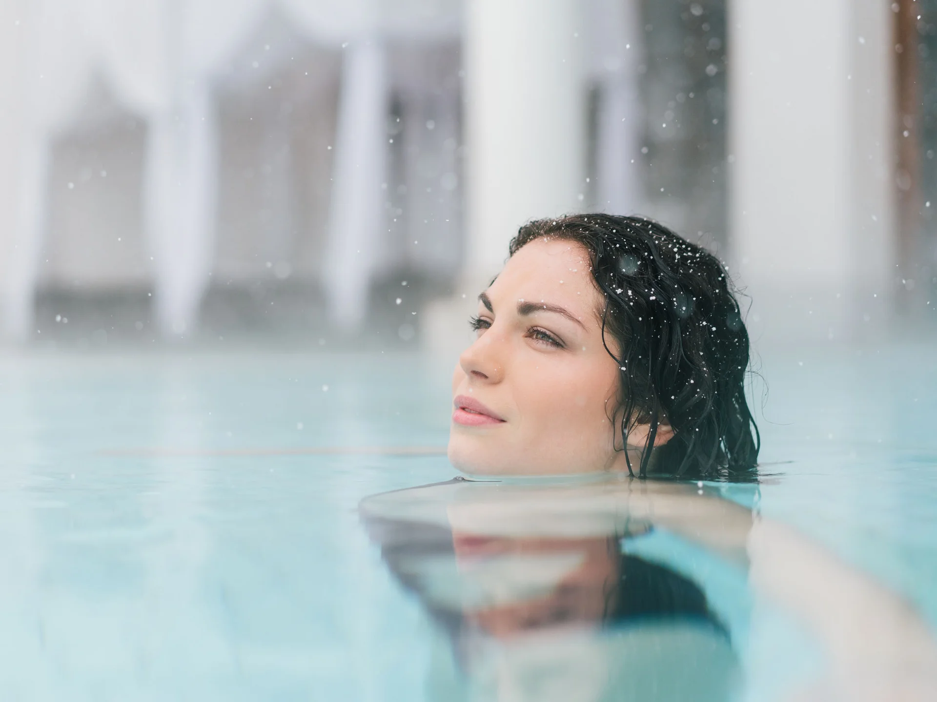 Bilder, die Sie sehen müssen. Frau entspannt im Wasser mit fallendem Schnee im Hintergrund