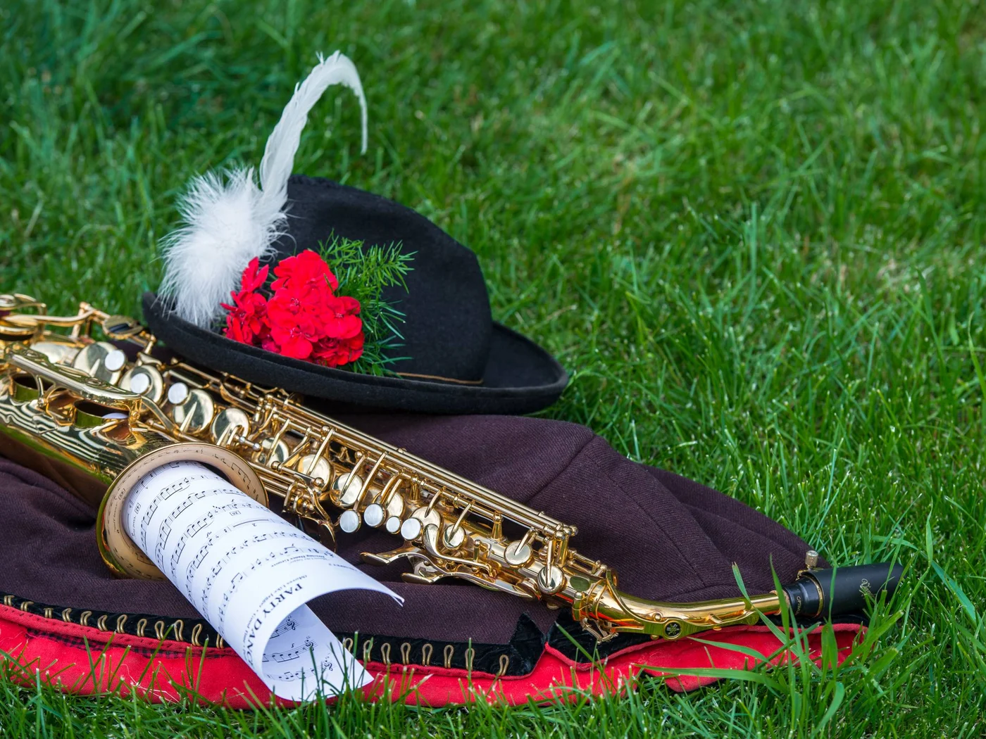 Die Schlossevents Saxophon, Notenblatt und Hut mit Feder und roten Blumen auf Gras