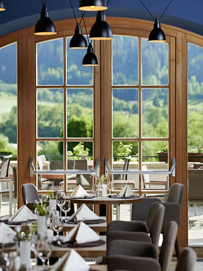 Mit der Familie ins Hotel? Tirol ist die richtige Wahl. Elegantes Restaurant mit gedeckten Tischen und Blick auf eine grüne Landschaft