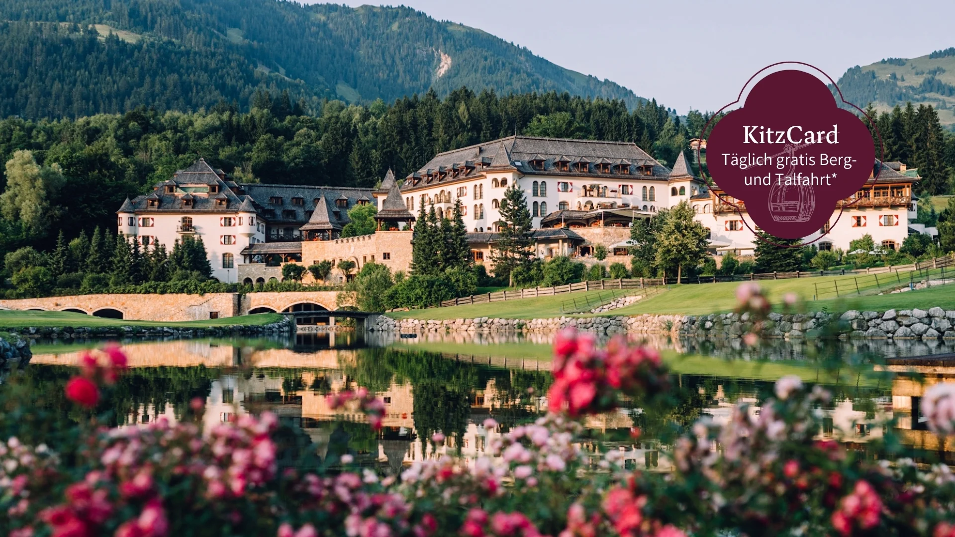 Schlosshotel Kitzbühel – ein Premiumerlebnis Hotelanlage am See vor bewaldeten Bergen mit blühenden Blumen im Vordergrund
